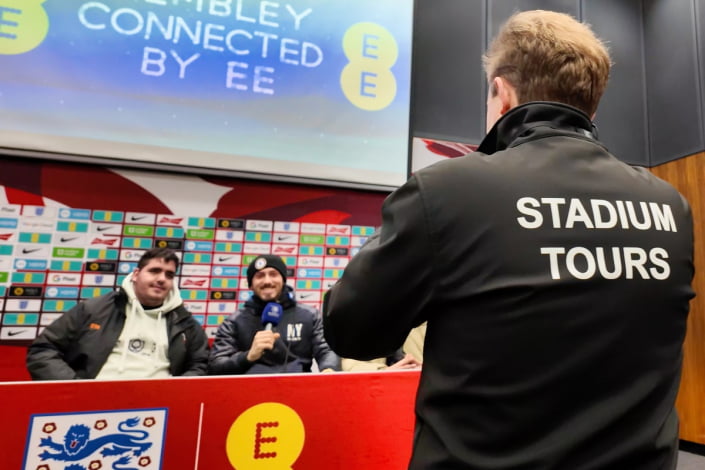 Wembley Stadium tour guide takes a photo of visitors in the press room