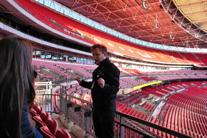 Wembley Stadium tour guide in the stands during a tour talking to visitors.